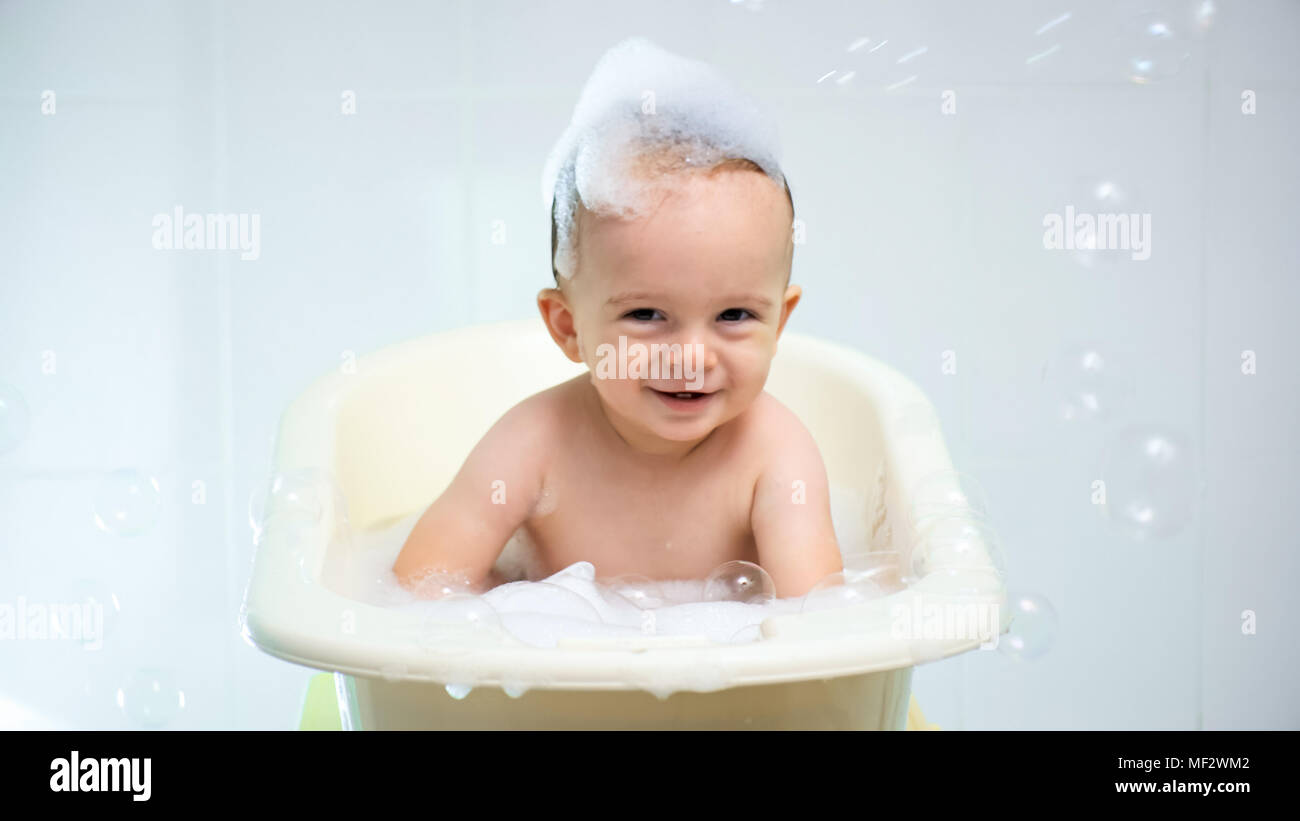 Portrait of cute smiling toddler boy sitting in bath with suds on head