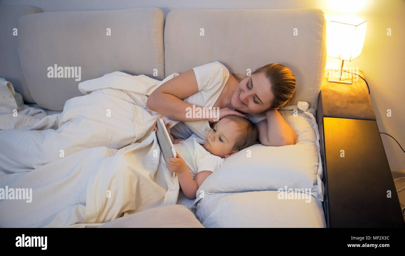 Cute Toddler Boy Holding Digital Tablet In Bed At Night With