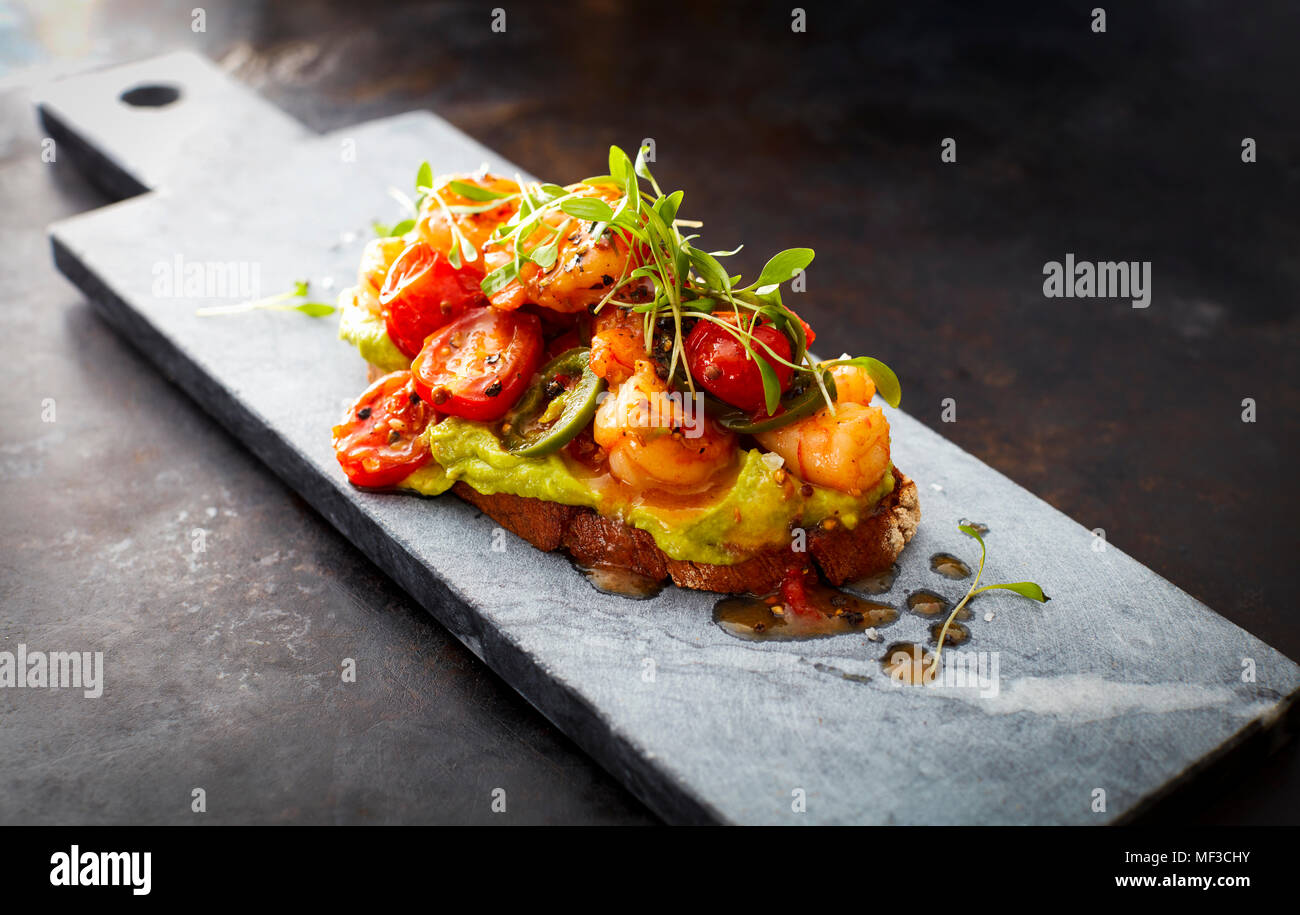Crostini with shrimps and tomatoes, roasted bread, herbs, avocado cream, sweet chili sauce, jalapenos, cress Stock Photo