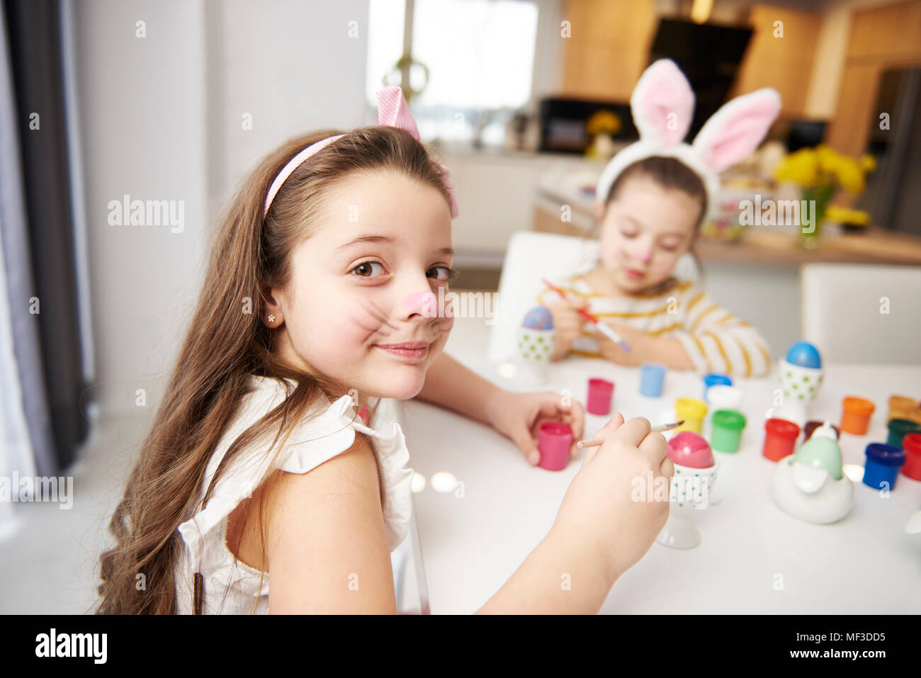 Portrait of smiling girl with sister sitting at table painting Easter eggs Stock Photo