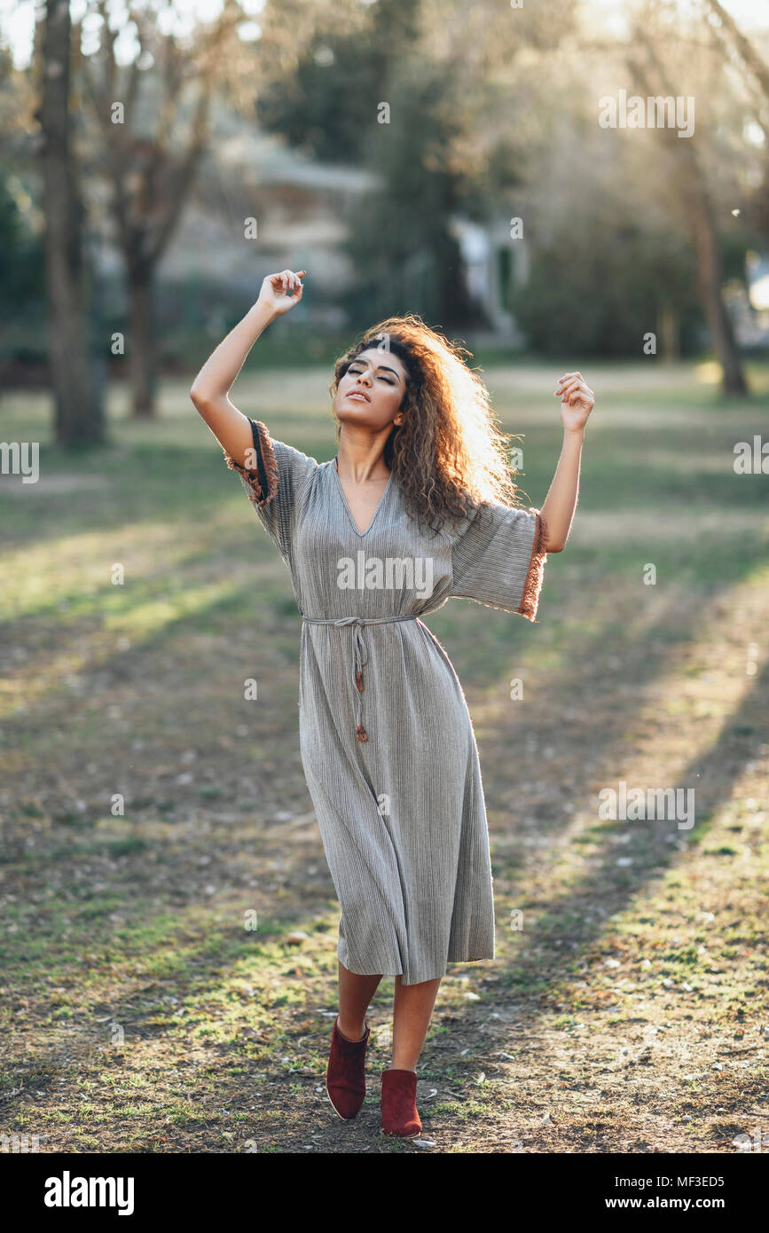 Spain, Andalusia, Granada. Happy young woman with curly hairstyle with open arms and closed eyes in an urban park. Lifestyle concept. Stock Photo