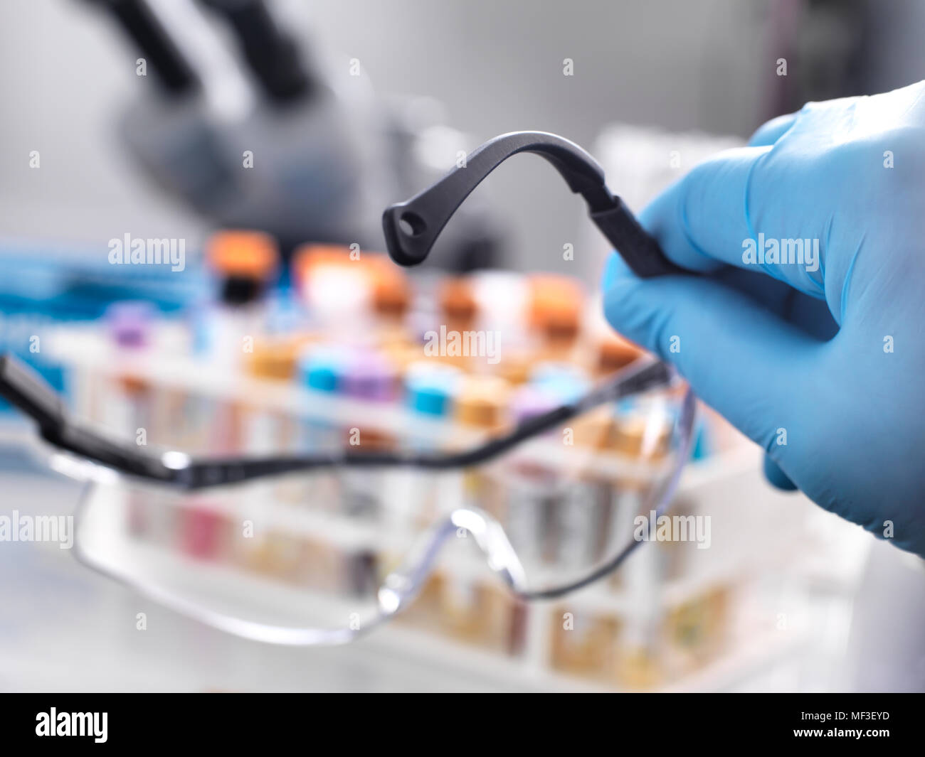 Medical technician holding protective glasses with human samples on the laboratory bench Stock Photo