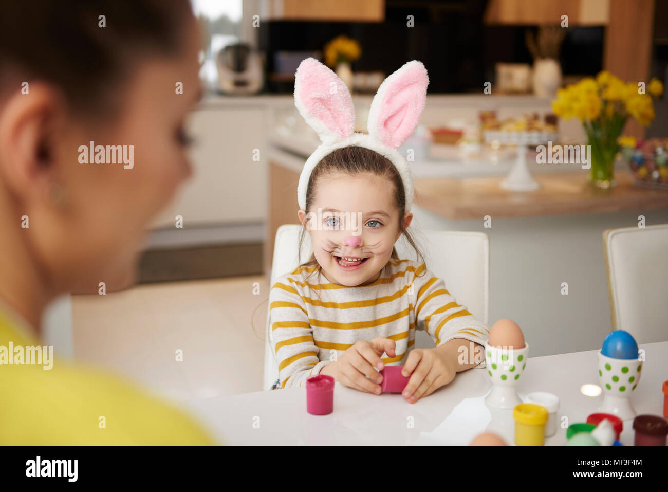 Girl with bunny ears and mother sitting at table with Easter eggs Stock Photo