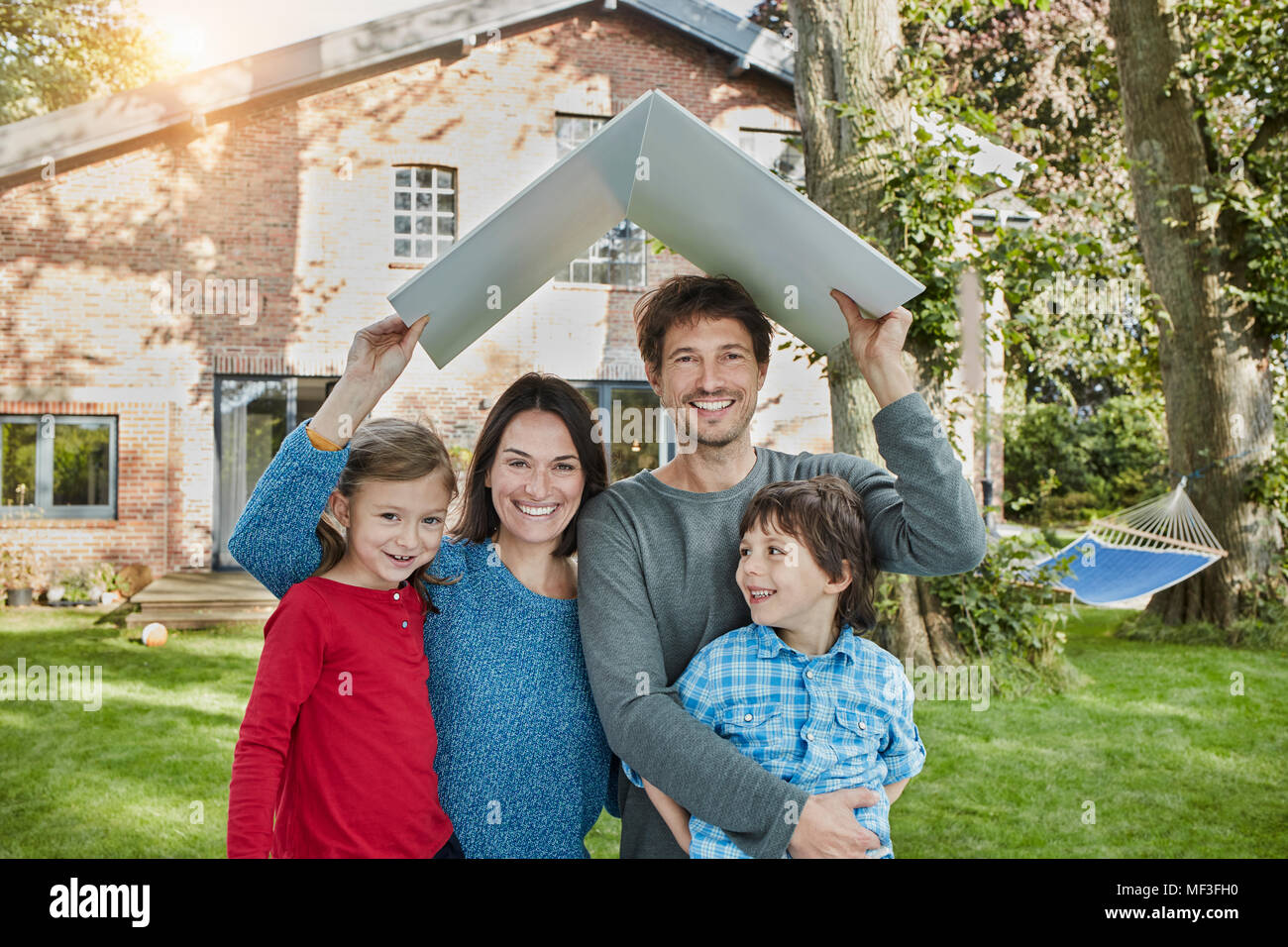 Portrait of happy family in garden of their home holding roof Stock Photo