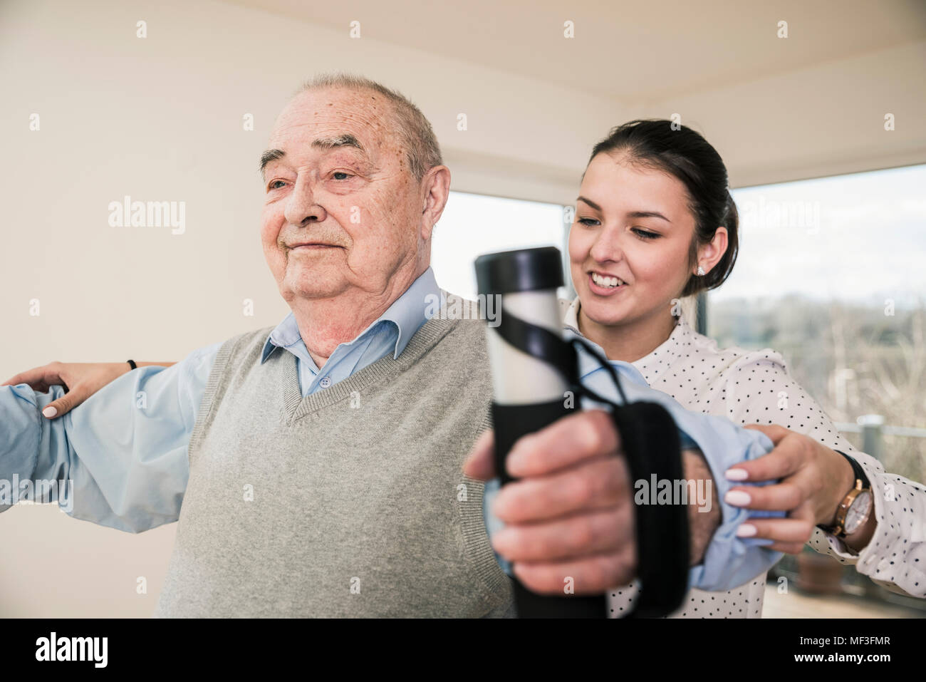 Young woman supporting senior man doing an arm exercise Stock Photo