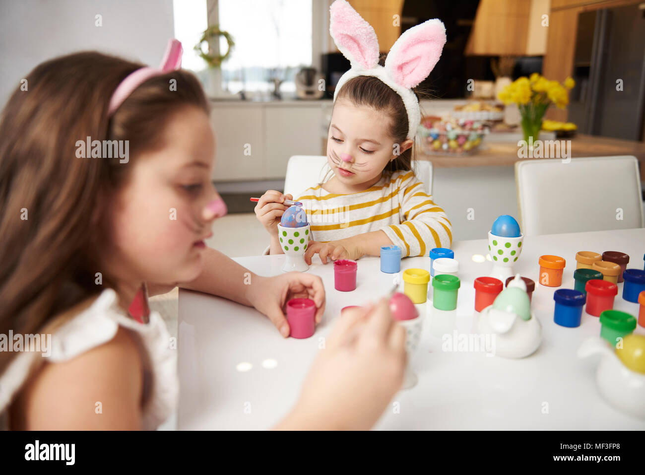 Sisters sitting at table painting Easter eggs Stock Photo