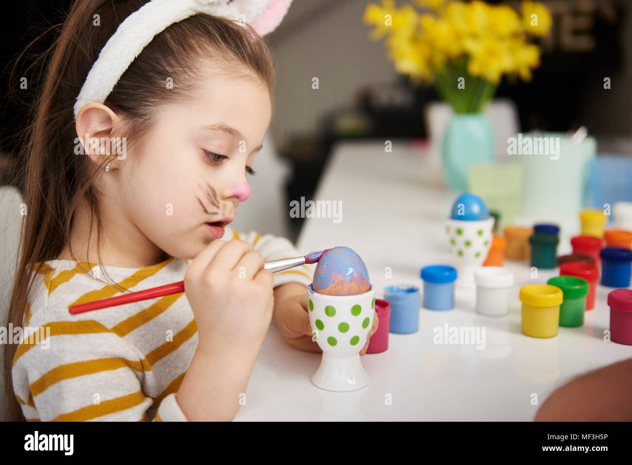 Girl with bunny ears sitting at table painting Easter eggs Stock Photo