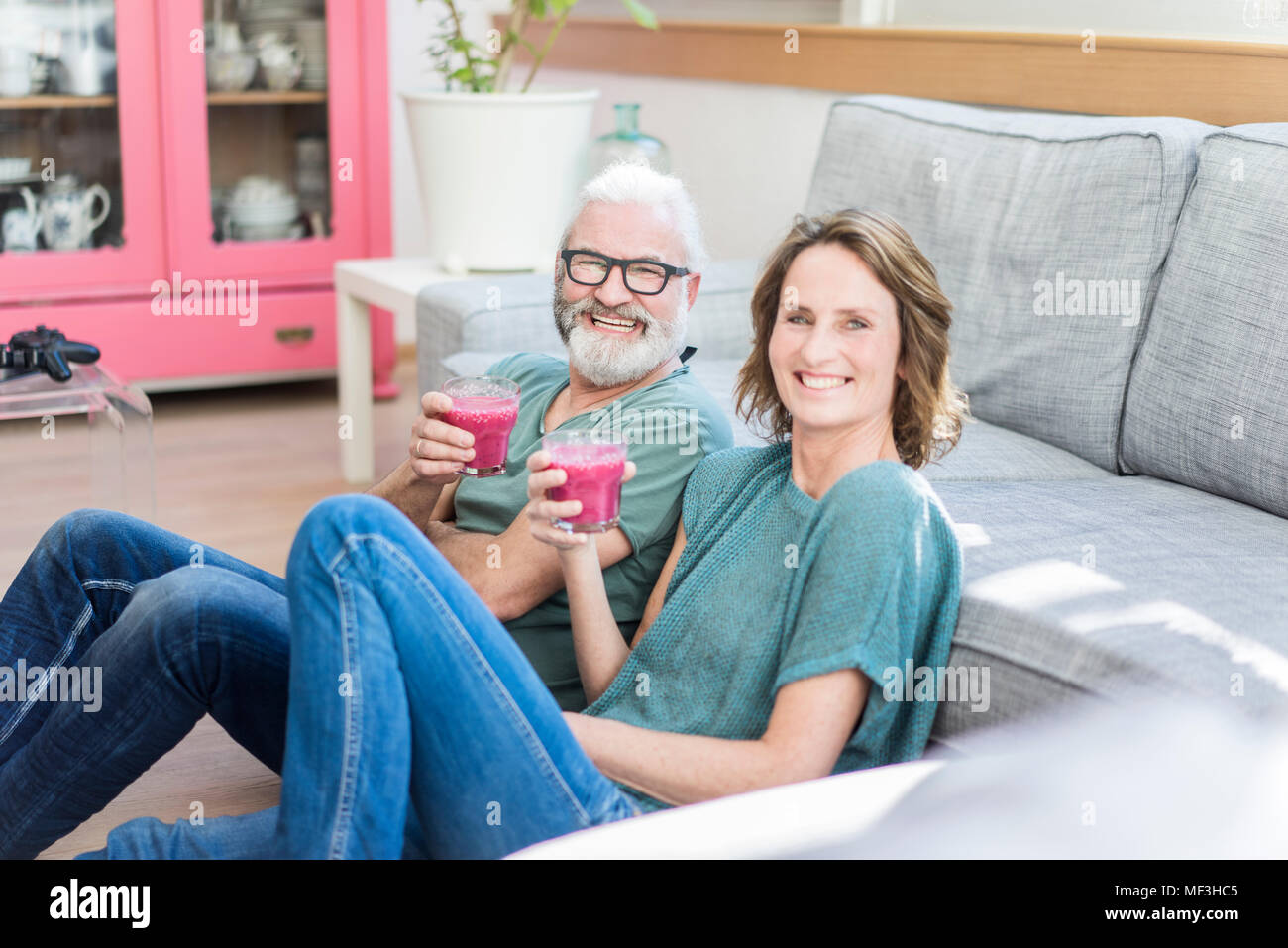 Happy mature couple with healthy drinks in living room at home Stock Photo