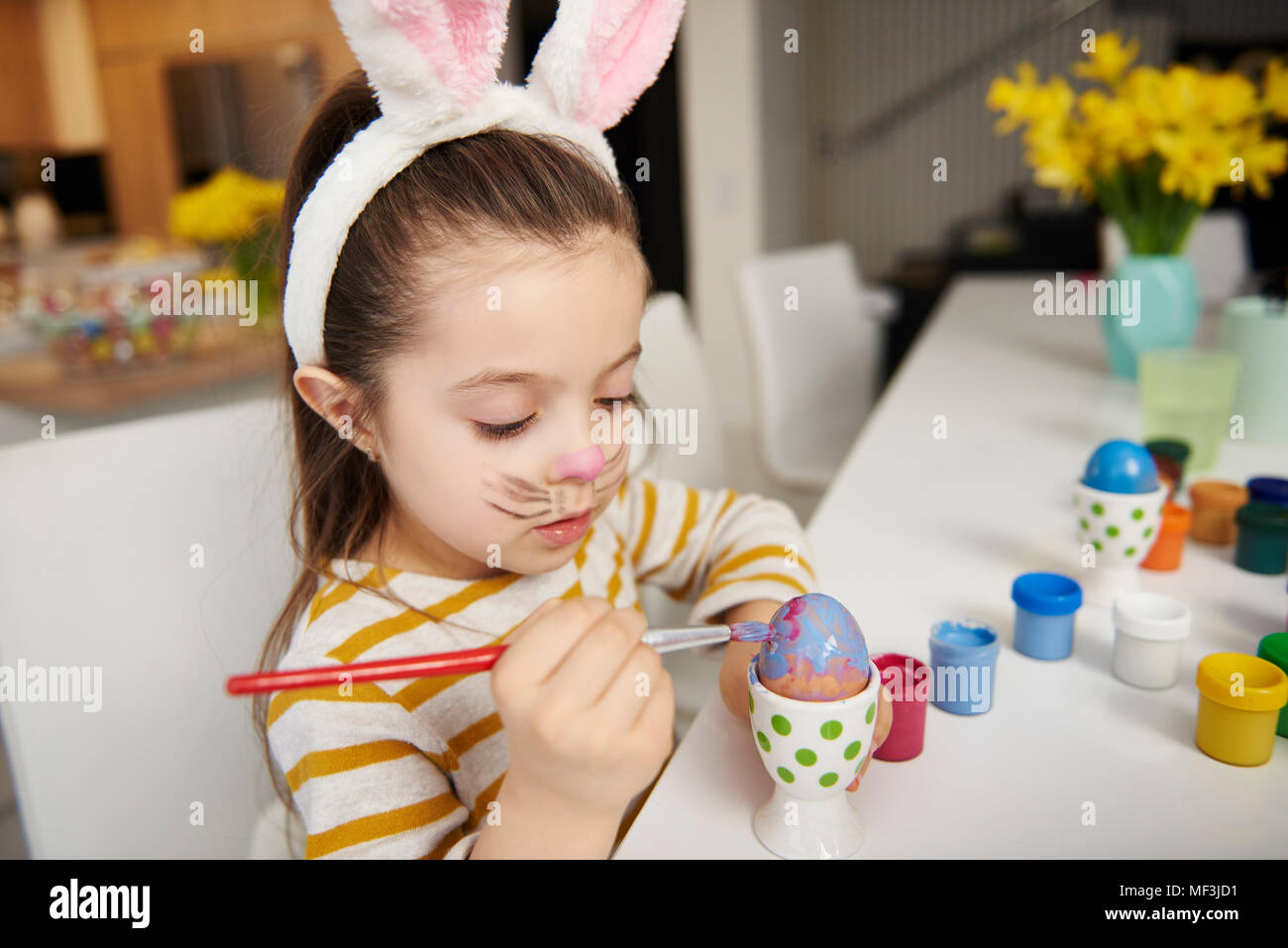 Girl with bunny ears sitting at table painting Easter eggs Stock Photo