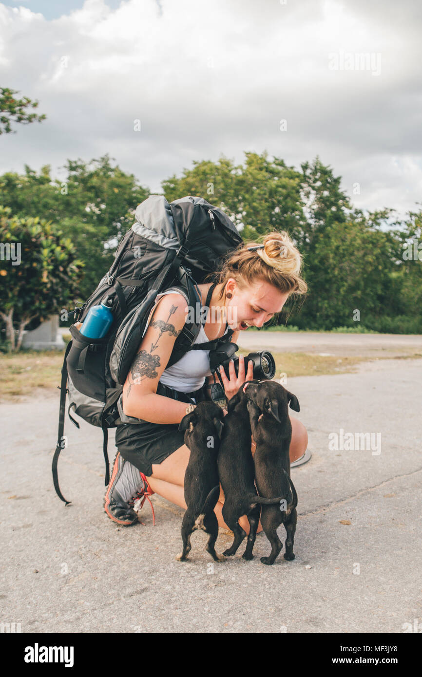 Cuba, young woman with backpack stroking young dogs, laughing Stock Photo