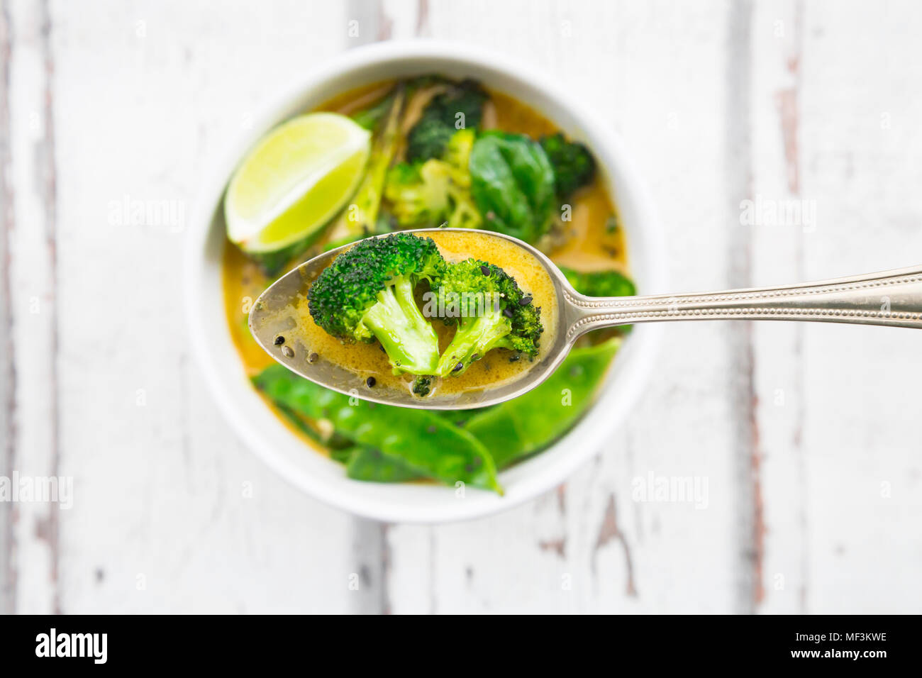 Green thai curry with broccoli, pak choi, snow peas, baby spinach, lime, broccoli and sauce on spoon Stock Photo