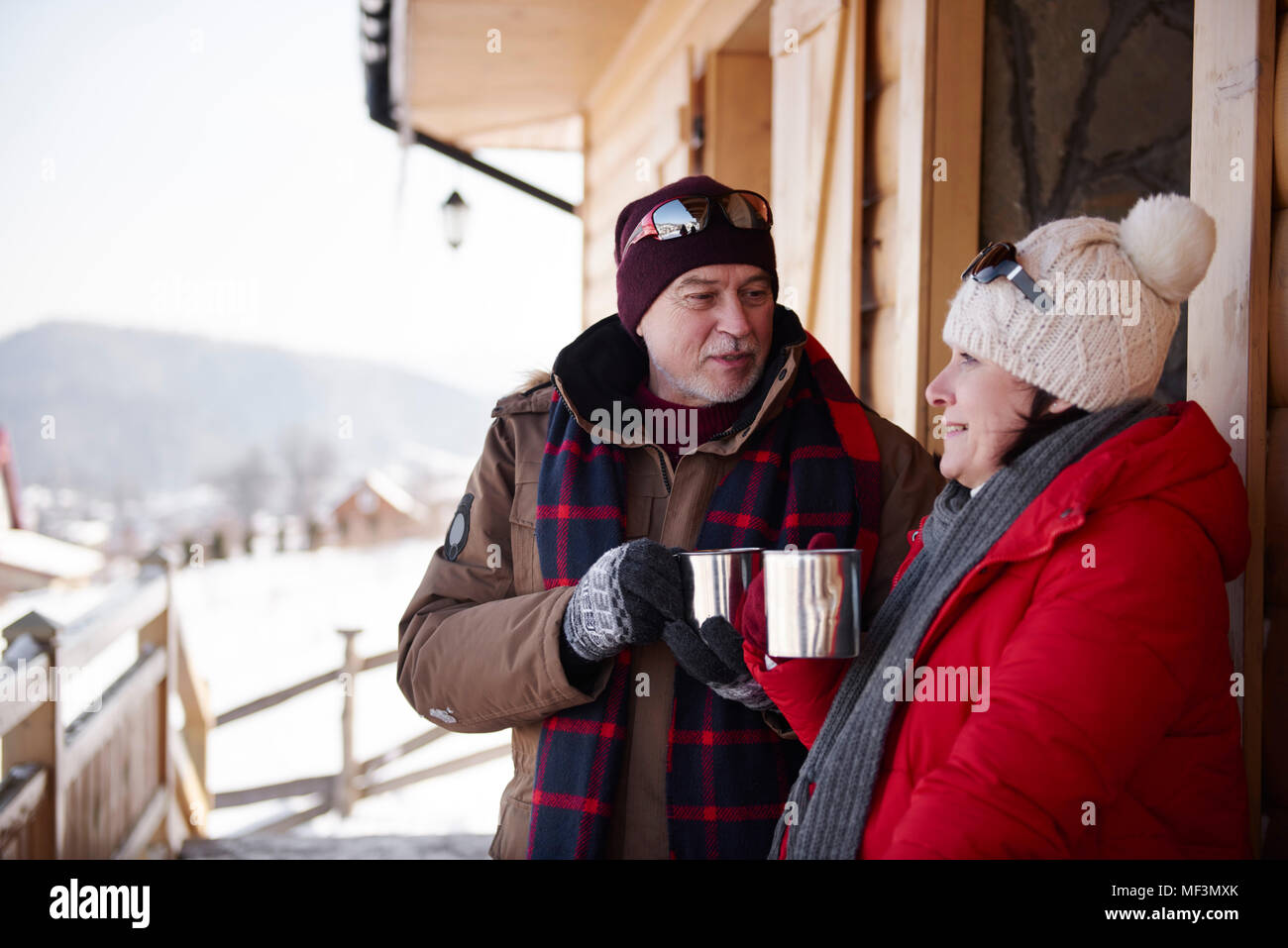 Mature couple with hot drinks talking outdoors at mountain hut  in winter Stock Photo