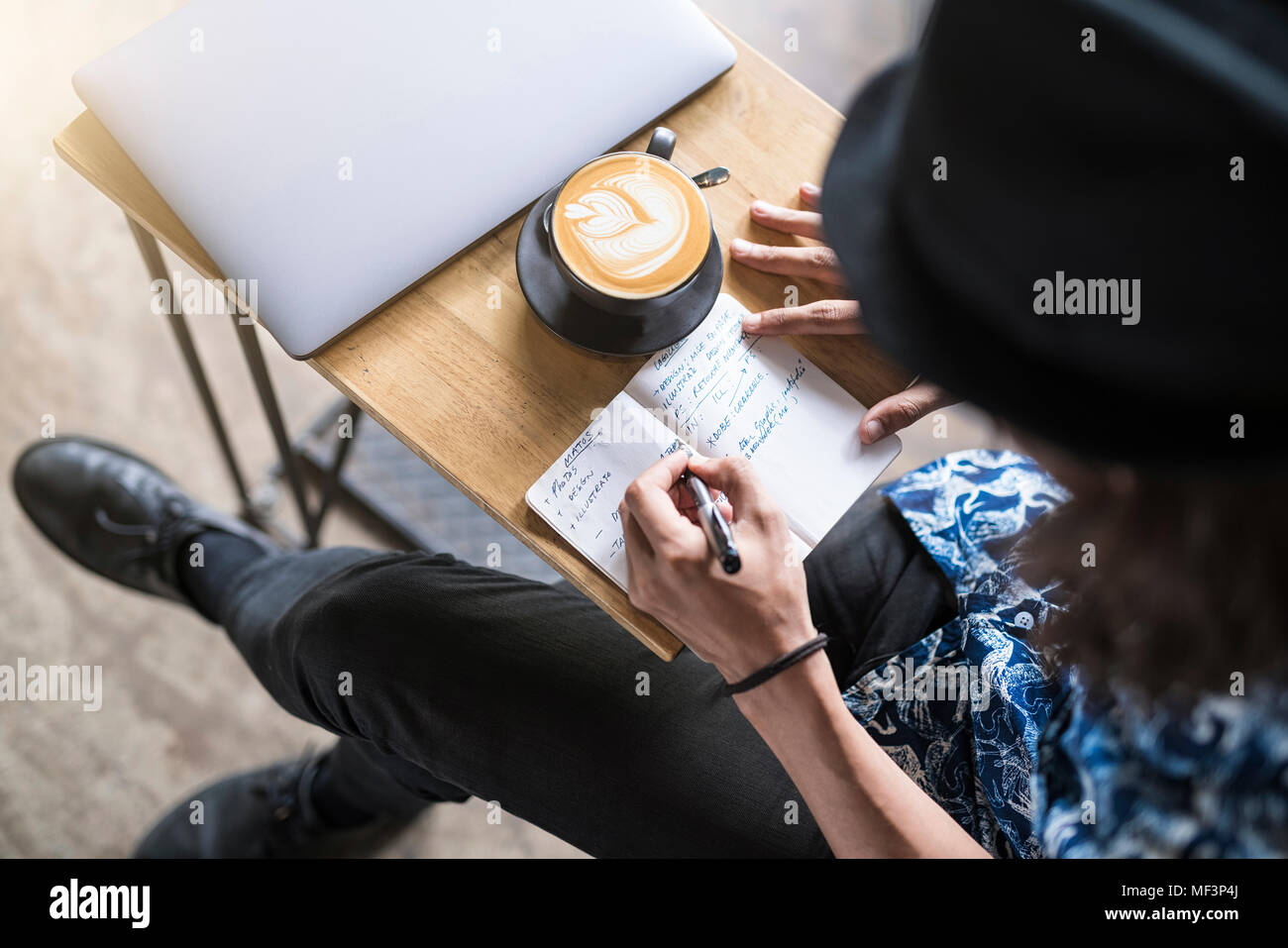 Artist writing into notebook in a cafe with coffee and laptop on the table Stock Photo