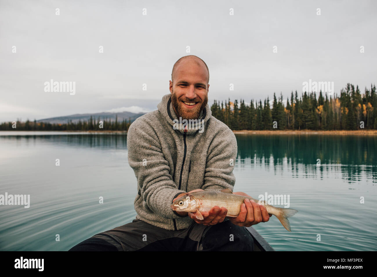 Canada, British Columbia, portrait of smiling man in canoe holding fish on Boya Lake Stock Photo