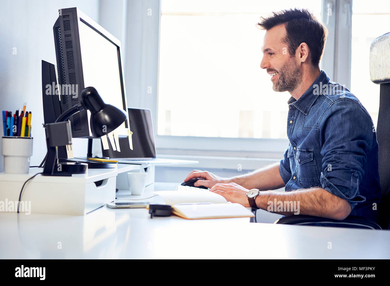 Smiling man working on computer at desk in office Stock Photo