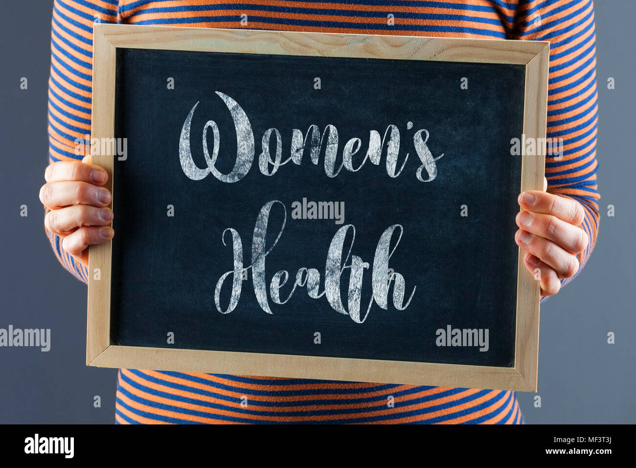 Female hands holding small black chalkboard in front of the body with text saying Women's Health Stock Photo