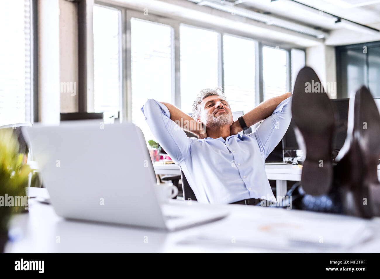 Relaxed mature businessman sitting at desk in office leaning back Stock