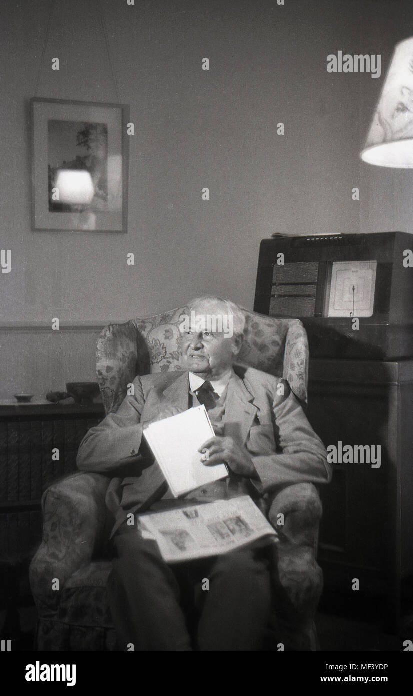 1948, historical, an elderly gentleman sitting in an armchair indoors with his newspaper and behind him, a large cabinet wireless or radio receiver, London, England, UK. Stock Photo