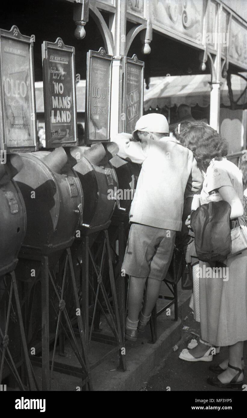 1940s, historical, young schoolboy using a mutoscope arcade movie viewer at a funfair, London, England, UK, with his mother looking on. These coin-operated machines contained a reel of still card pictures that fliped thereby giving an animated movie or film. Stock Photo