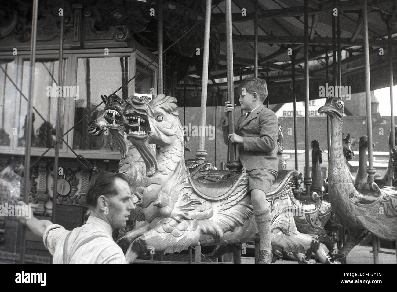 1948, young boy wearing school uniform riding a wooden dragon on a fun fair merry-go-round, London, England, Uk. Stock Photo