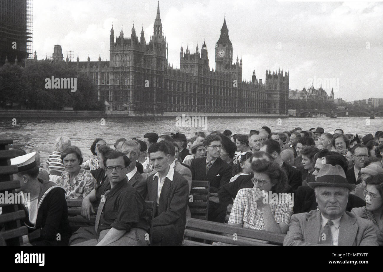 1950s, historical picture from this era of a group of people sitting on a boat enjoying a river cruise along the river Thames as they go pass the iconic London building, the Palace of Westminster, the British Houses of Parliament, the government of the UK in the background. Stock Photo