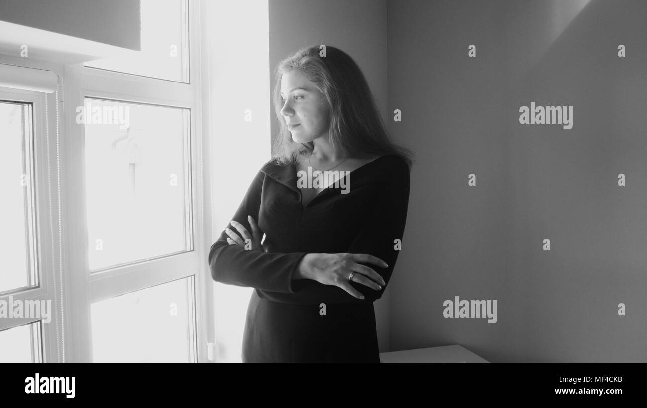 Black and white image of young elegant woman looking out of big window Stock Photo