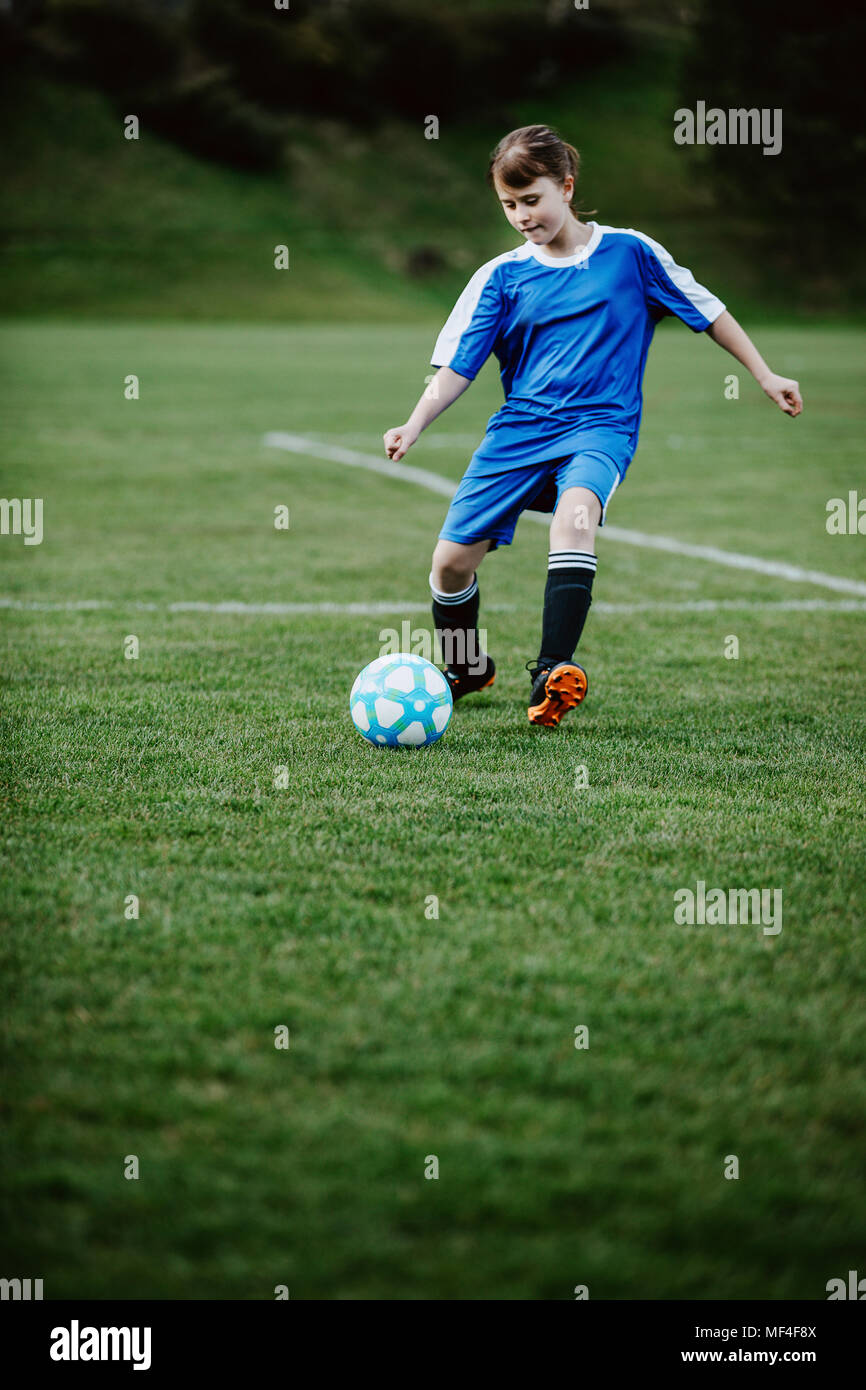 Teen girl playing soccer at local stadium outside on grass field