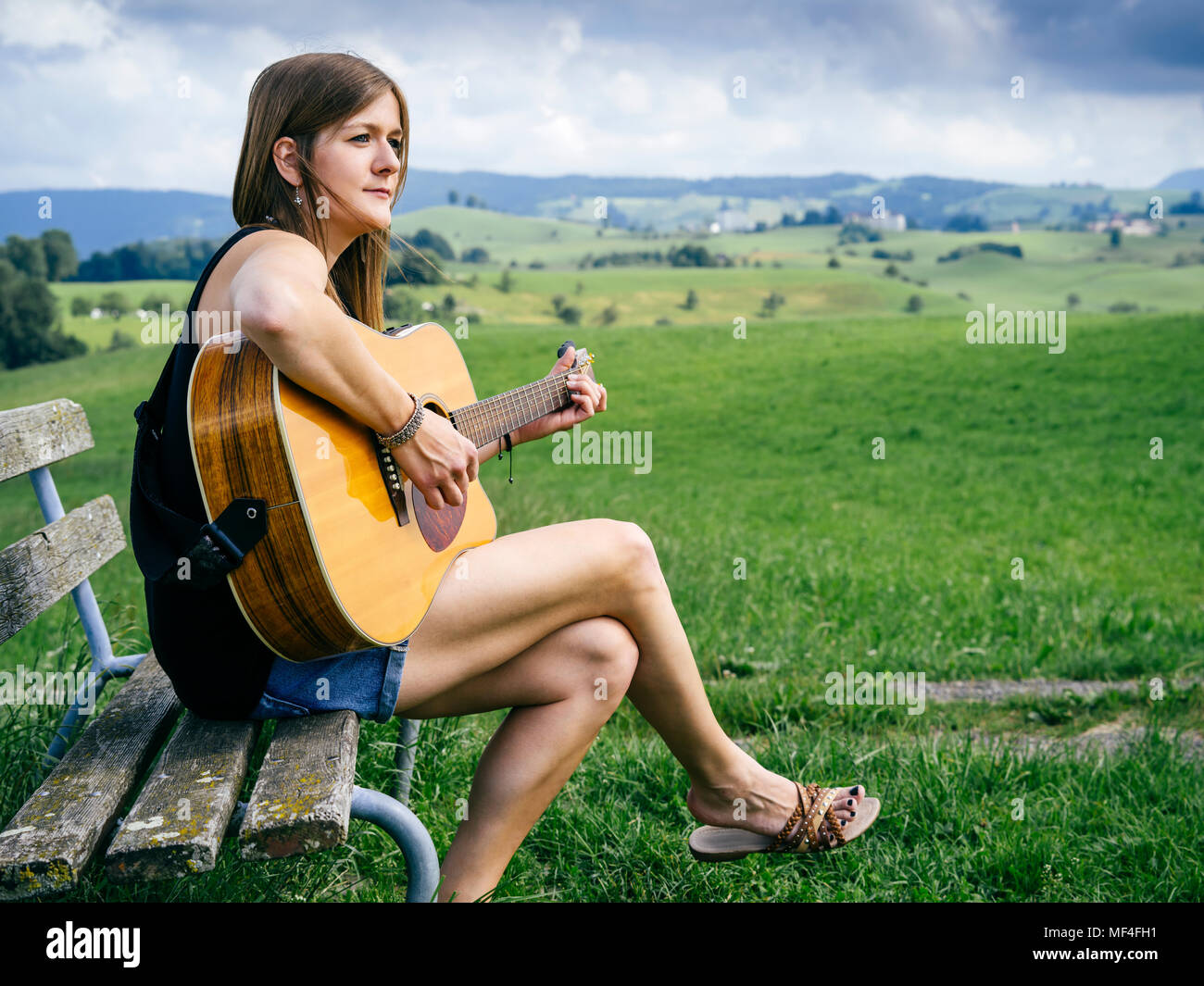 Photo of a young woman playing acoustic guitar on a park bench Stock ...
