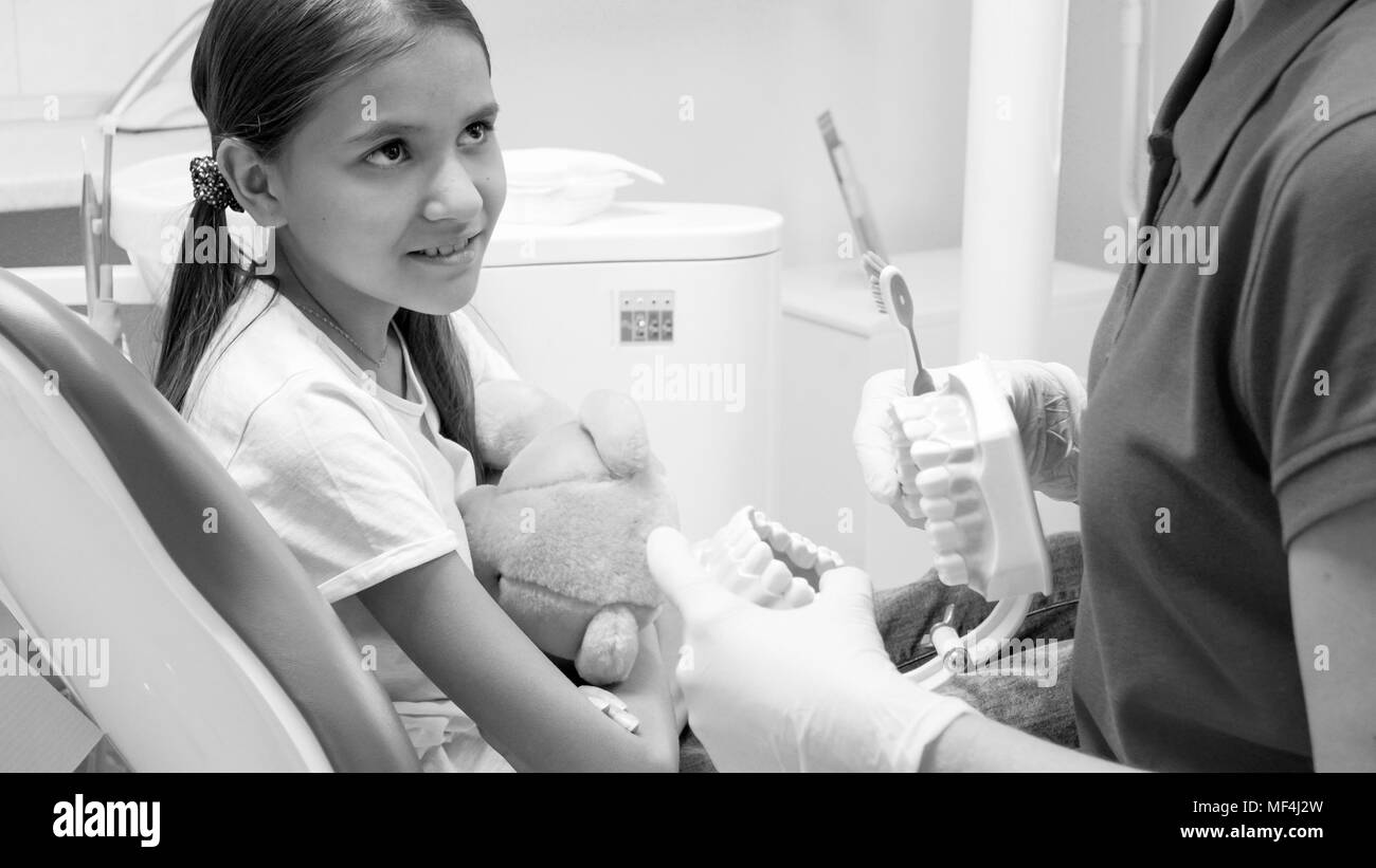 Black and white image of pediatric dentist educating little girl about