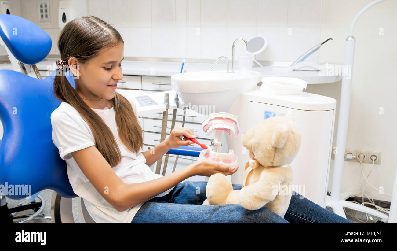 Portrait of smiling girl teaching her teddy bear cleaning teeth in dentist office Stock Photo