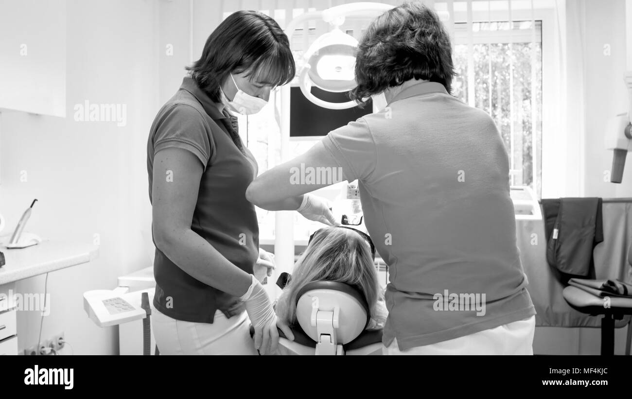Black and white image of dentist and assistant working with woman sitting in dentist chair Stock Photo