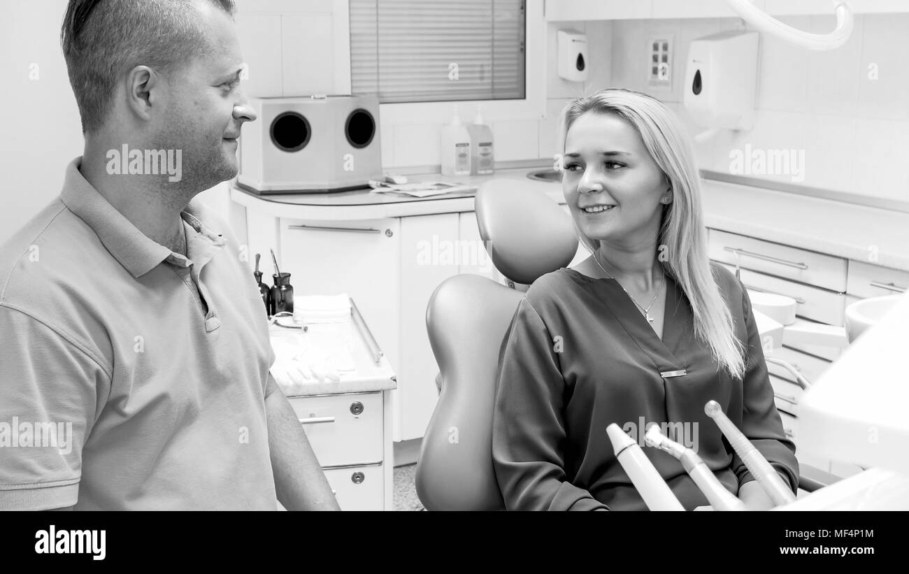 Black and white image of beautiful smiling woman sitting in dentist chair at clinic Stock Photo