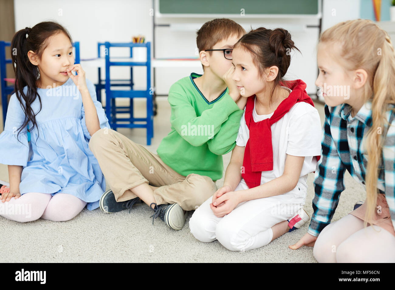 Primary school kids whispering words to each other while playing telephone game in classroom after lessons Stock Photo