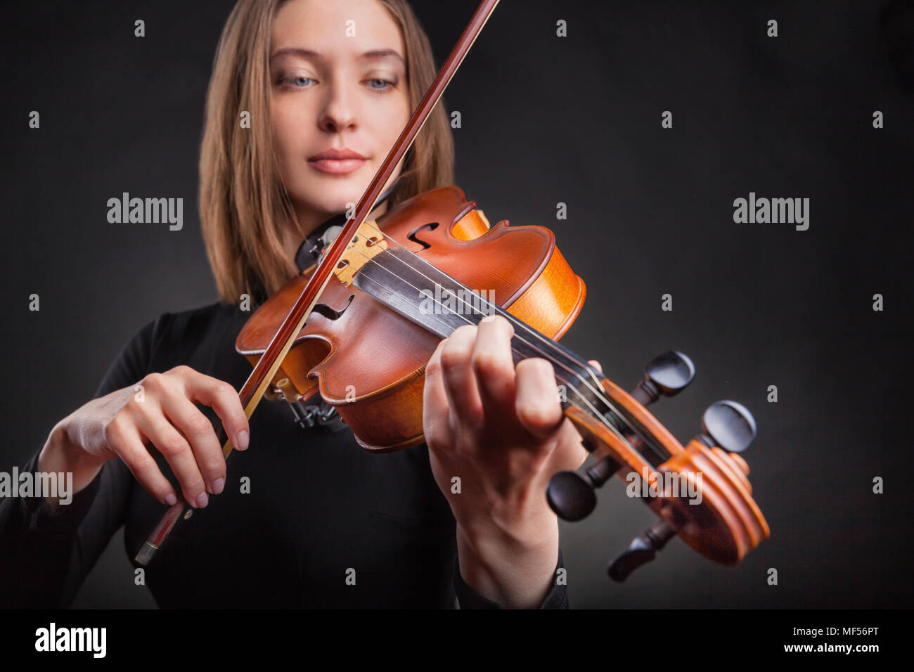 Beautiful young woman playing the violin on dark background Stock Photo