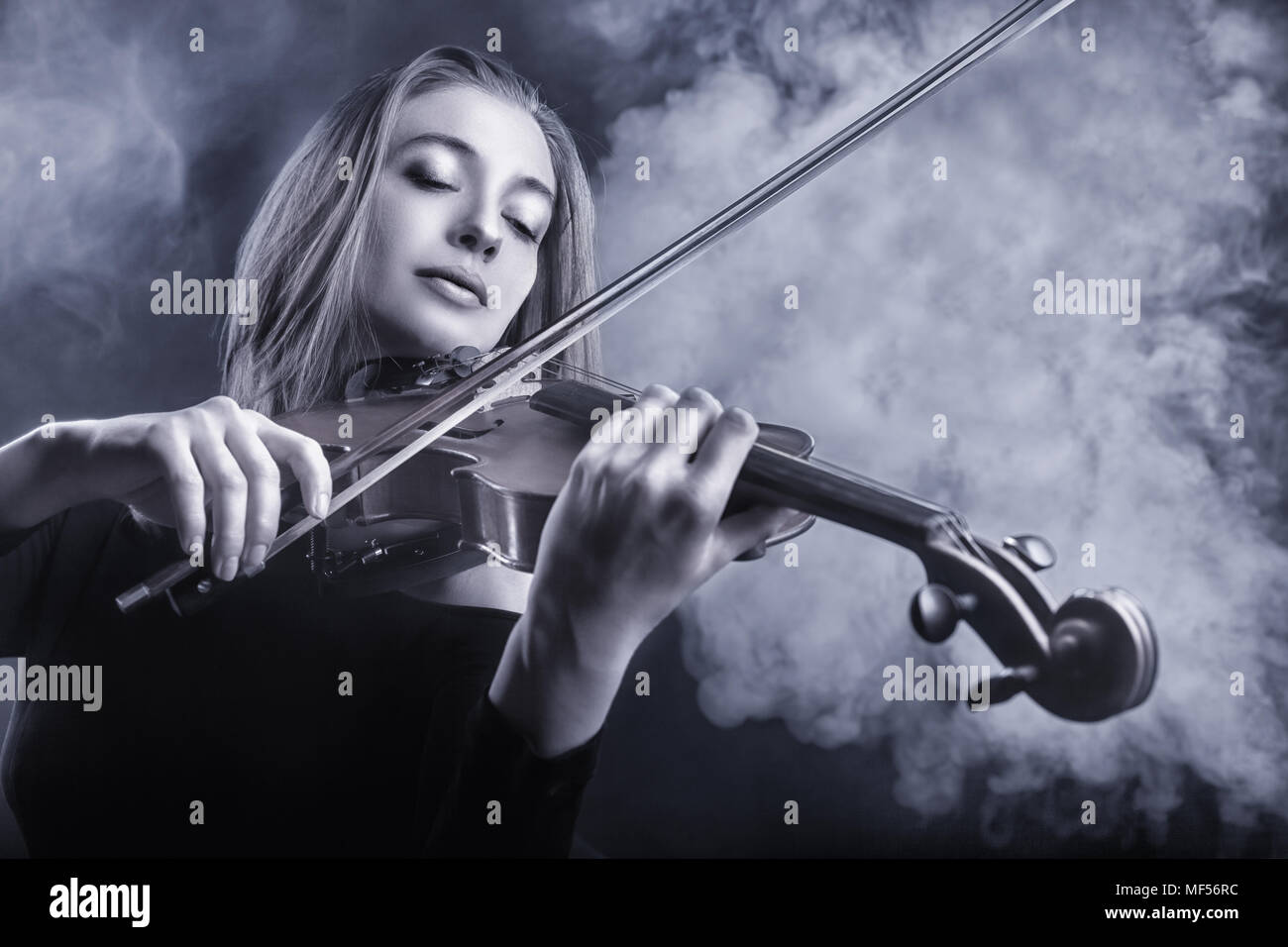 Black and white image. Beautiful young woman playing the violin. Fog in the background. Studio shot Stock Photo