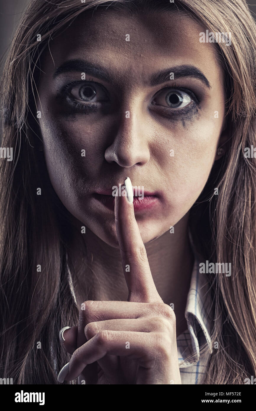 Domestic violence concept. Young woman with finger over her mouth Stock Photo