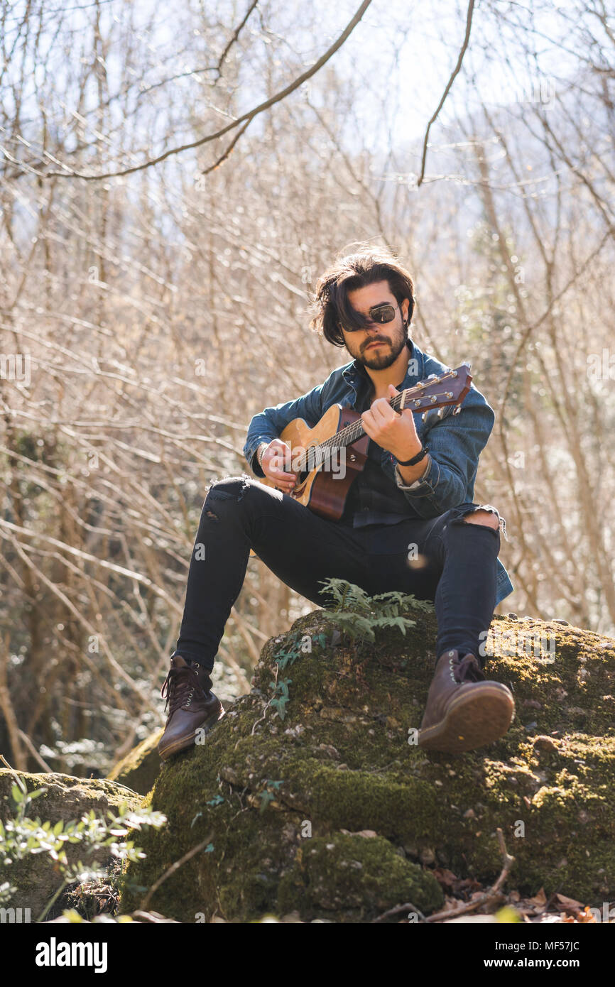 Young man sitting on rock playing guitar Stock Photo