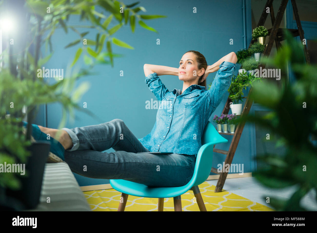 Beautiful woman sitting in her home, decorated with plants, daydreaming Stock Photo
