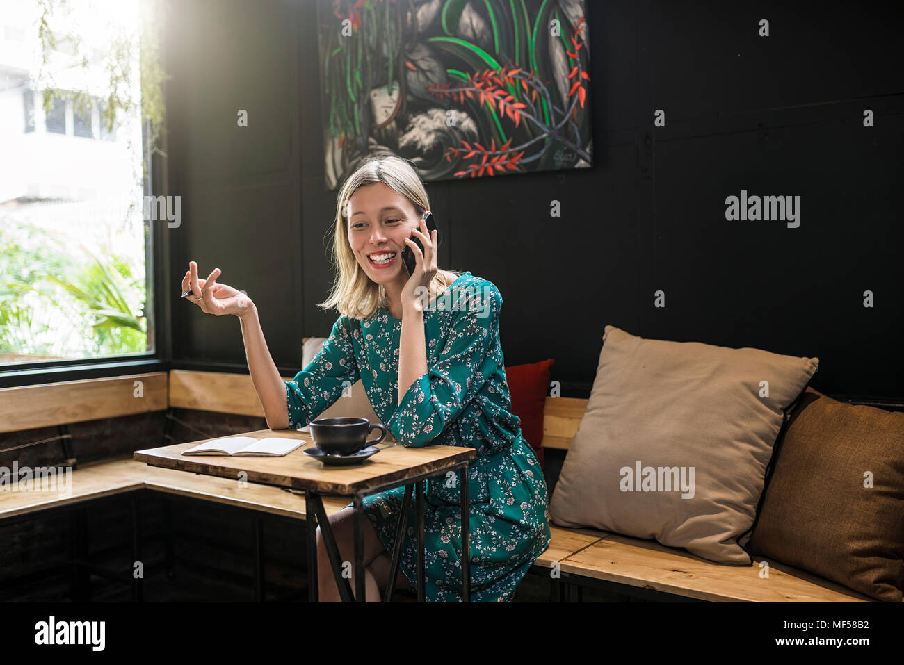 Young smiling woman with green dress sitting in cafe, talking to someone on her smartphone Stock Photo