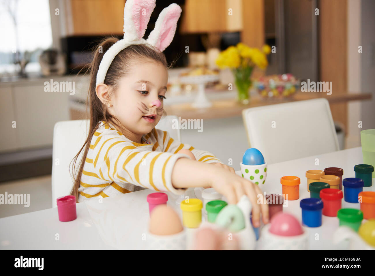 Girl with bunny ears sitting at table painting Easter eggs Stock Photo