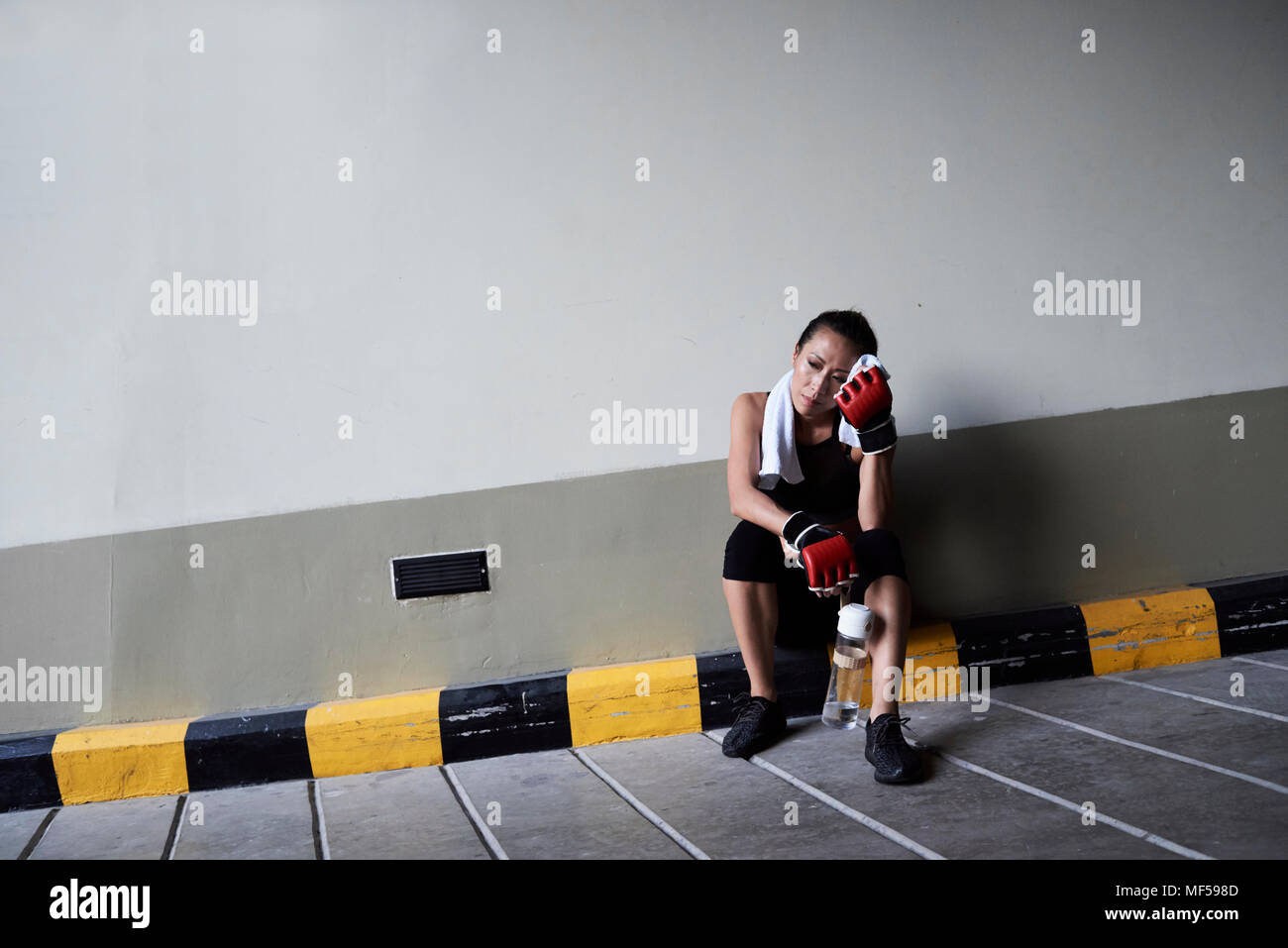 Female boxer sitting in a garage holding a towel Stock Photo