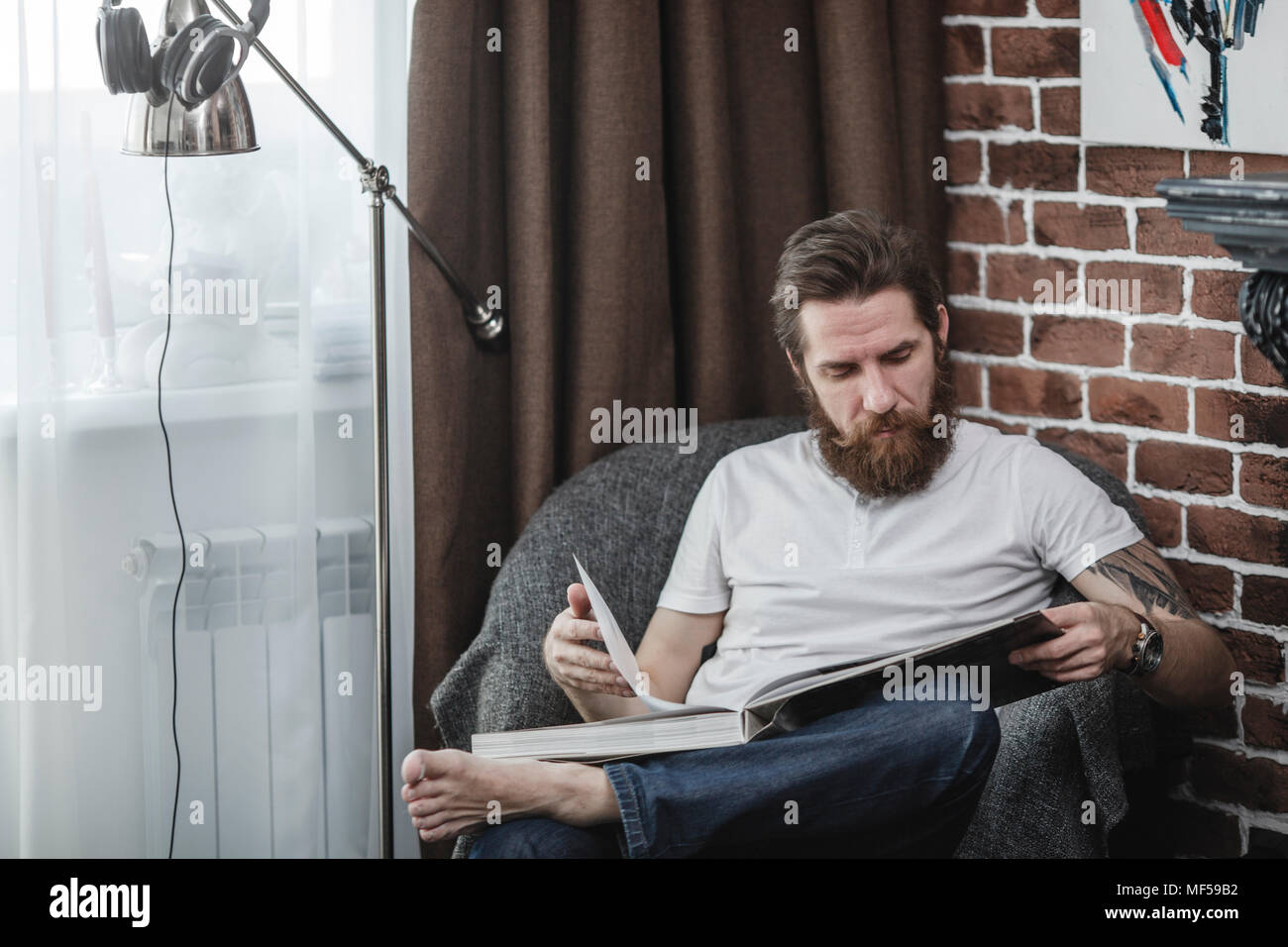 Man sitting on armchair looking at coffee-table book Stock Photo