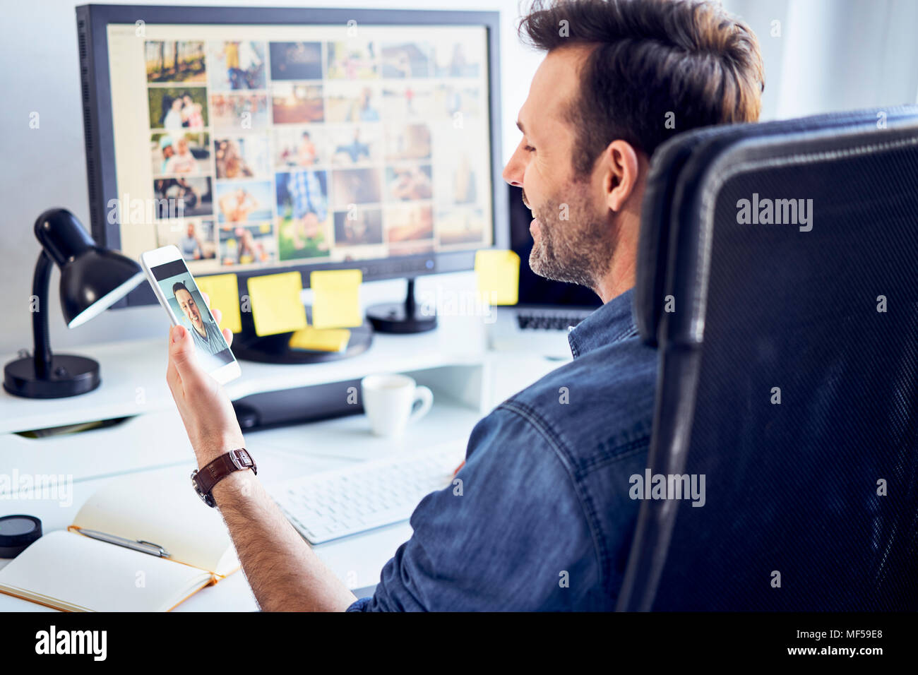 Photo editor at desk in office having video chat on his phone Stock Photo