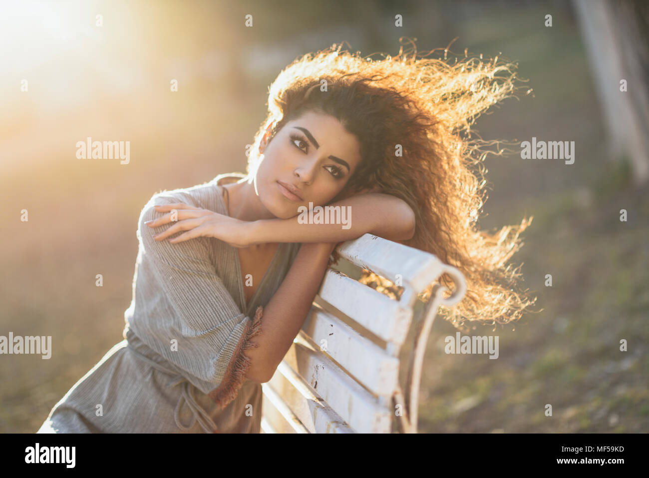Spain, Andalusia, Granada. Beautiful young woman with curly hairstyle sitting on a bench in an urban park. Lifestyle concept. Stock Photo
