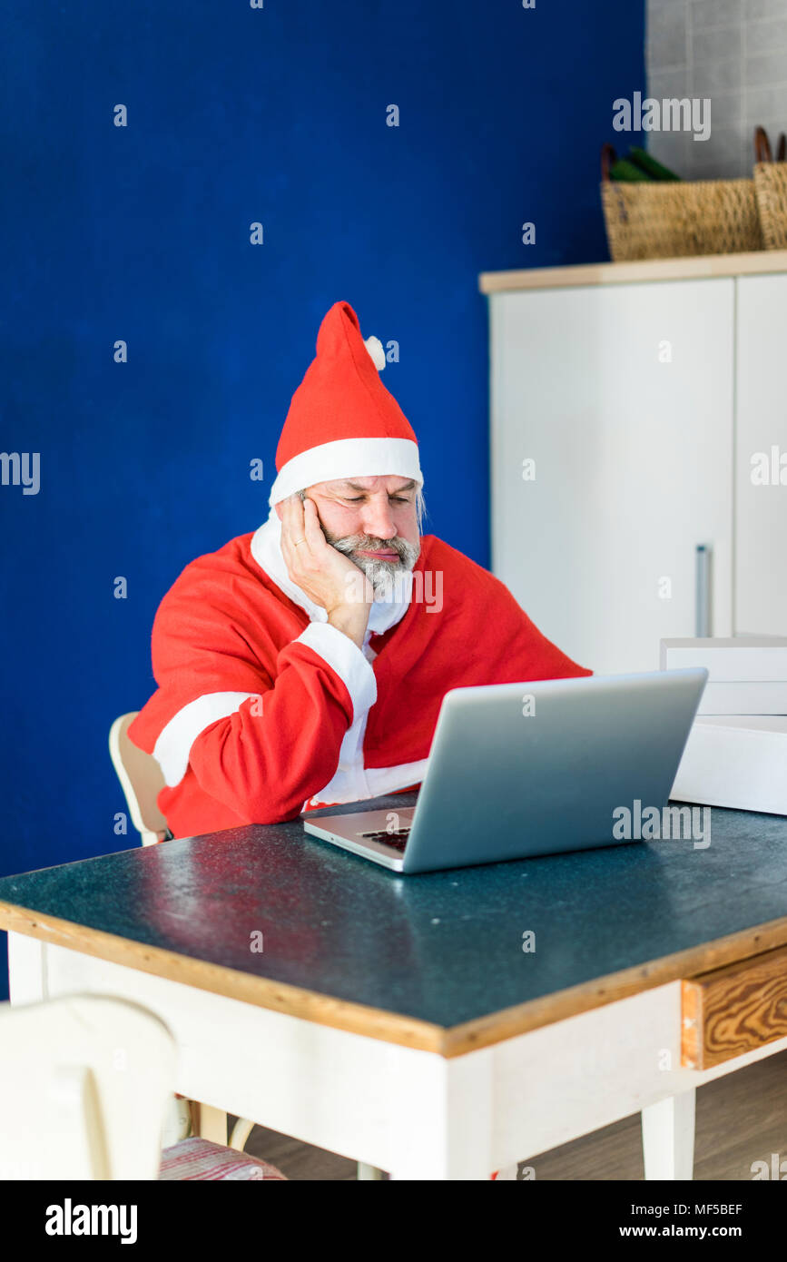 Frustrated Santa using laptop at home Stock Photo
