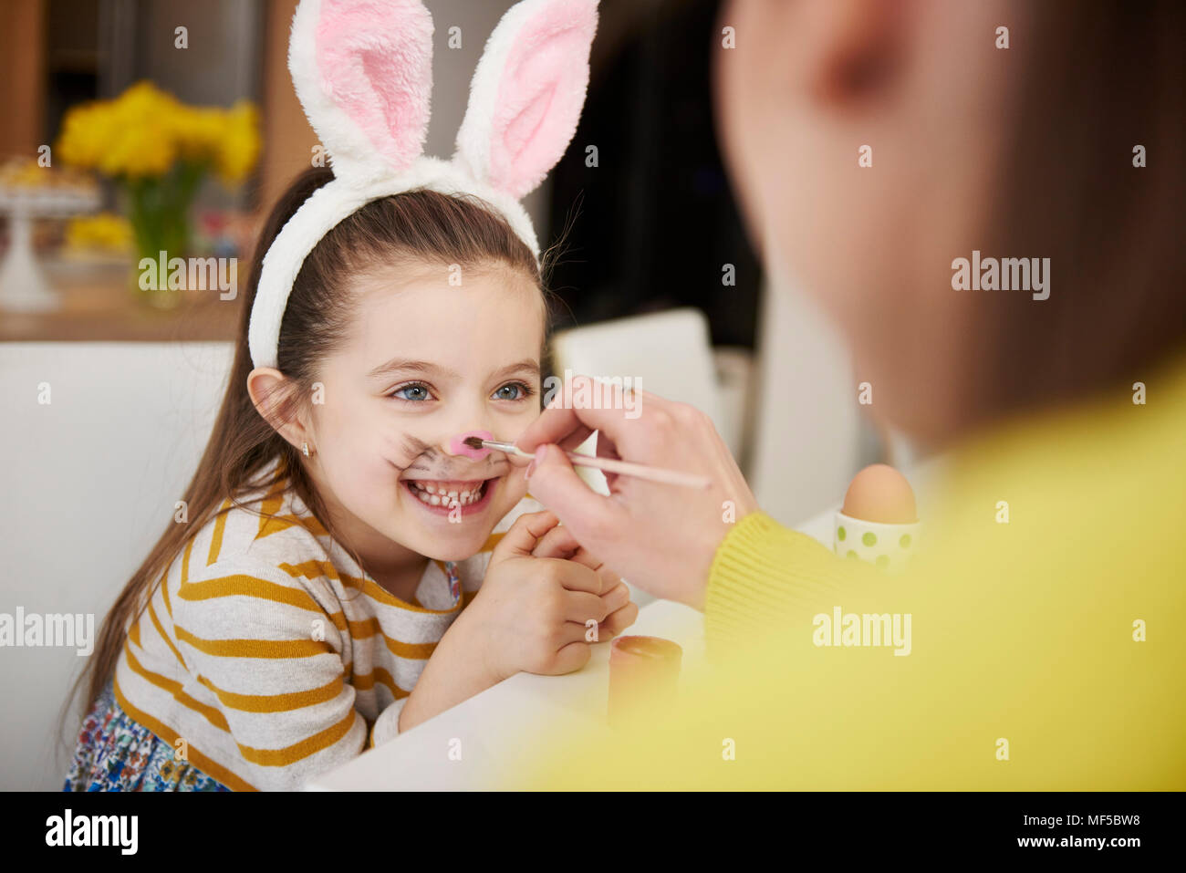 Mother painting daughter's face wearing bunny ears Stock Photo