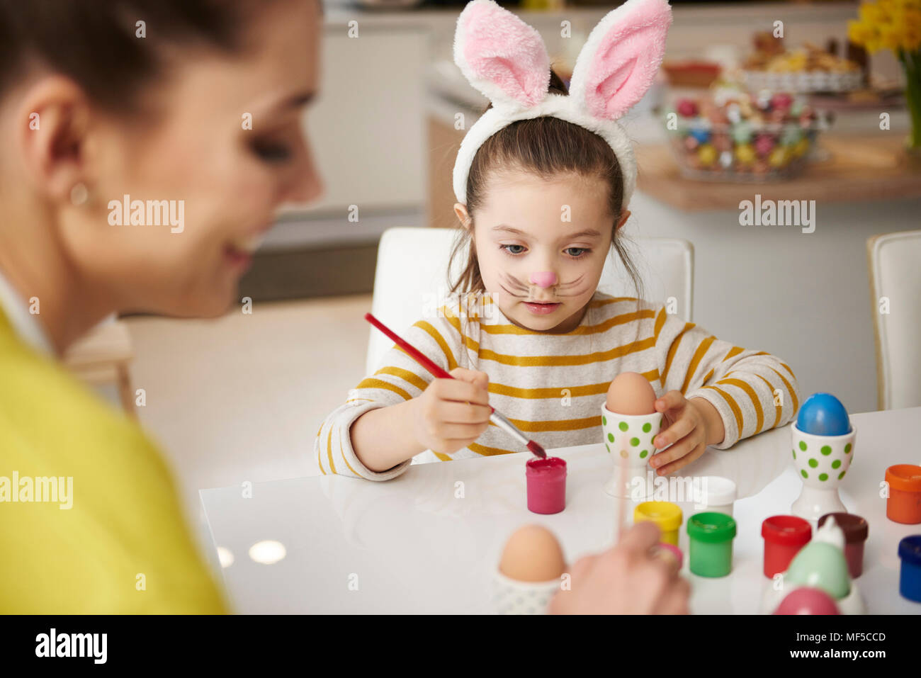 Mother and daughter with bunny ears sitting at table painting Easter eggs Stock Photo