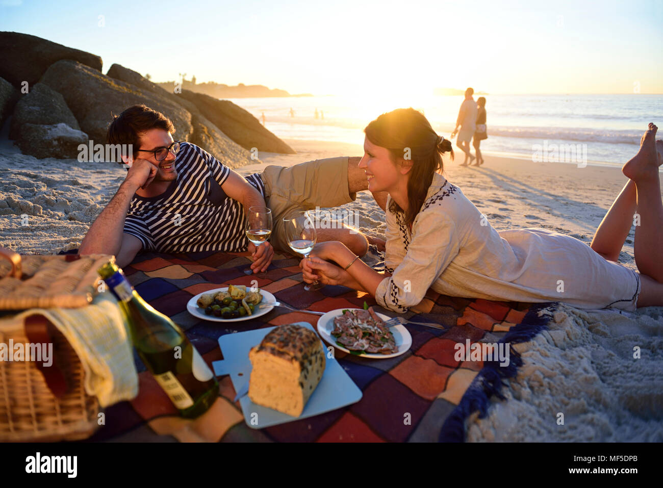 Happy couple having a picnic on the beach at sunset Stock Photo