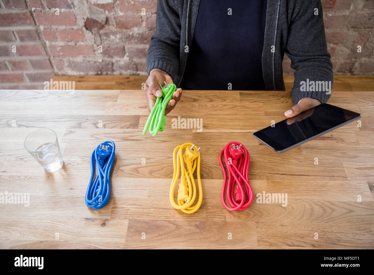 Businessman with tablet choosing from coloured power cables on table top, partial view Stock Photo