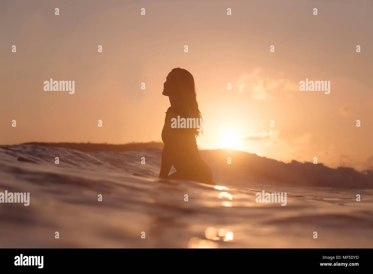 Indonesia, Lombok, female surfer sitting on surfboard at sunset Stock Photo
